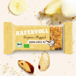 HAFERVOLL Organic Flapjack Banana & Brazil Nut 60g – Riegel in der Verpackung mit Bananenchips und Paranüssen